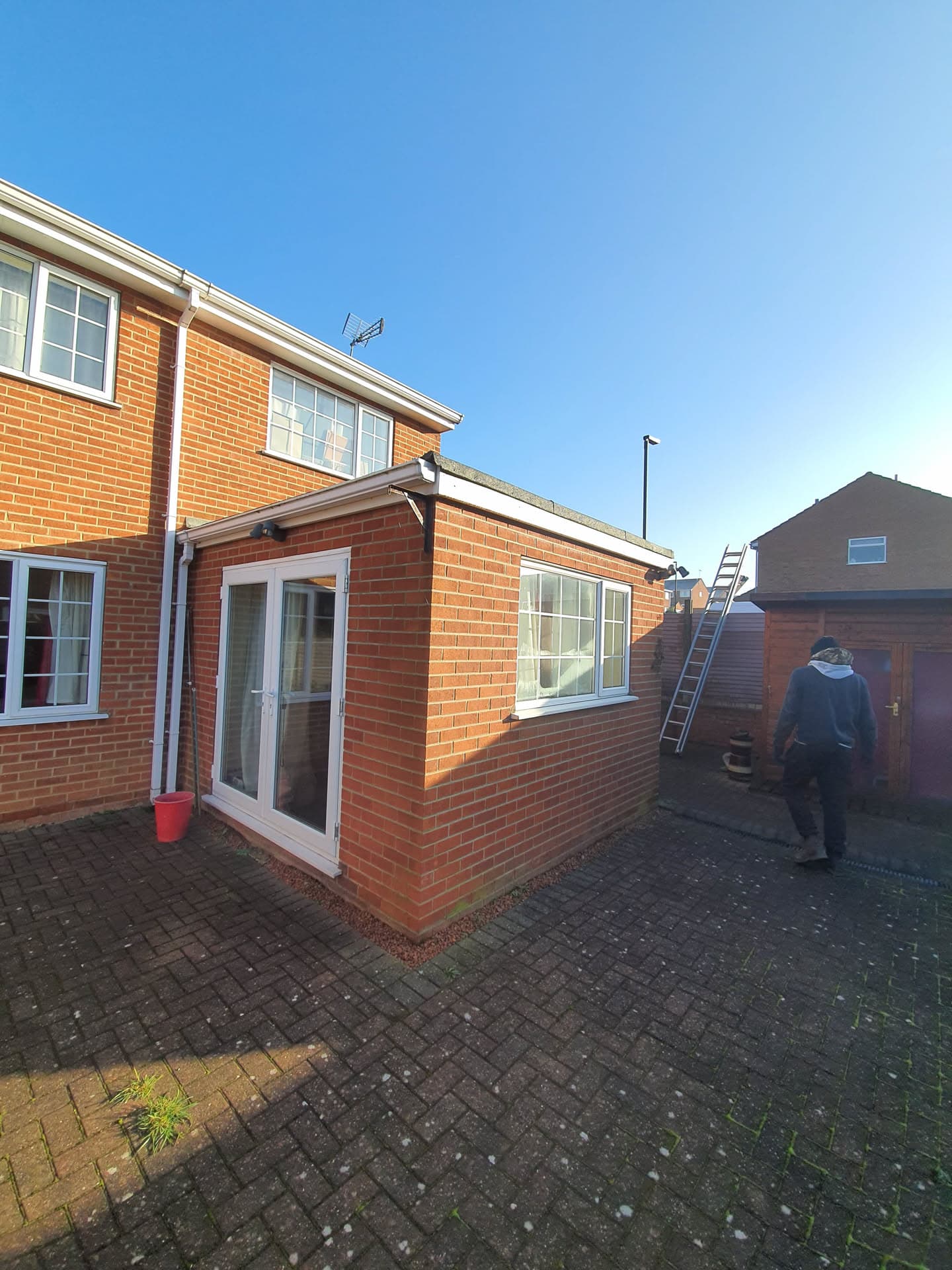 Flat roof installation on single-storey extension with white fascias and guttering, fitter working