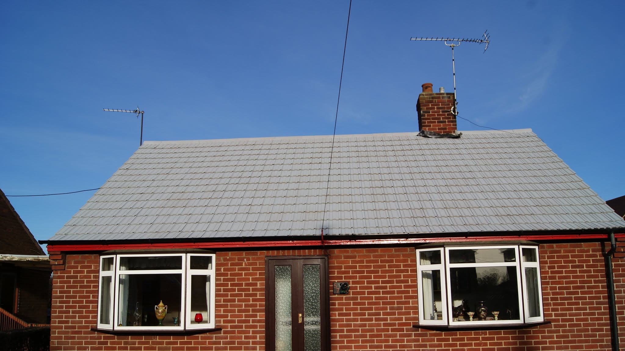Pitched roof with grey concrete tiles and brick chimney stack on red brick bungalow