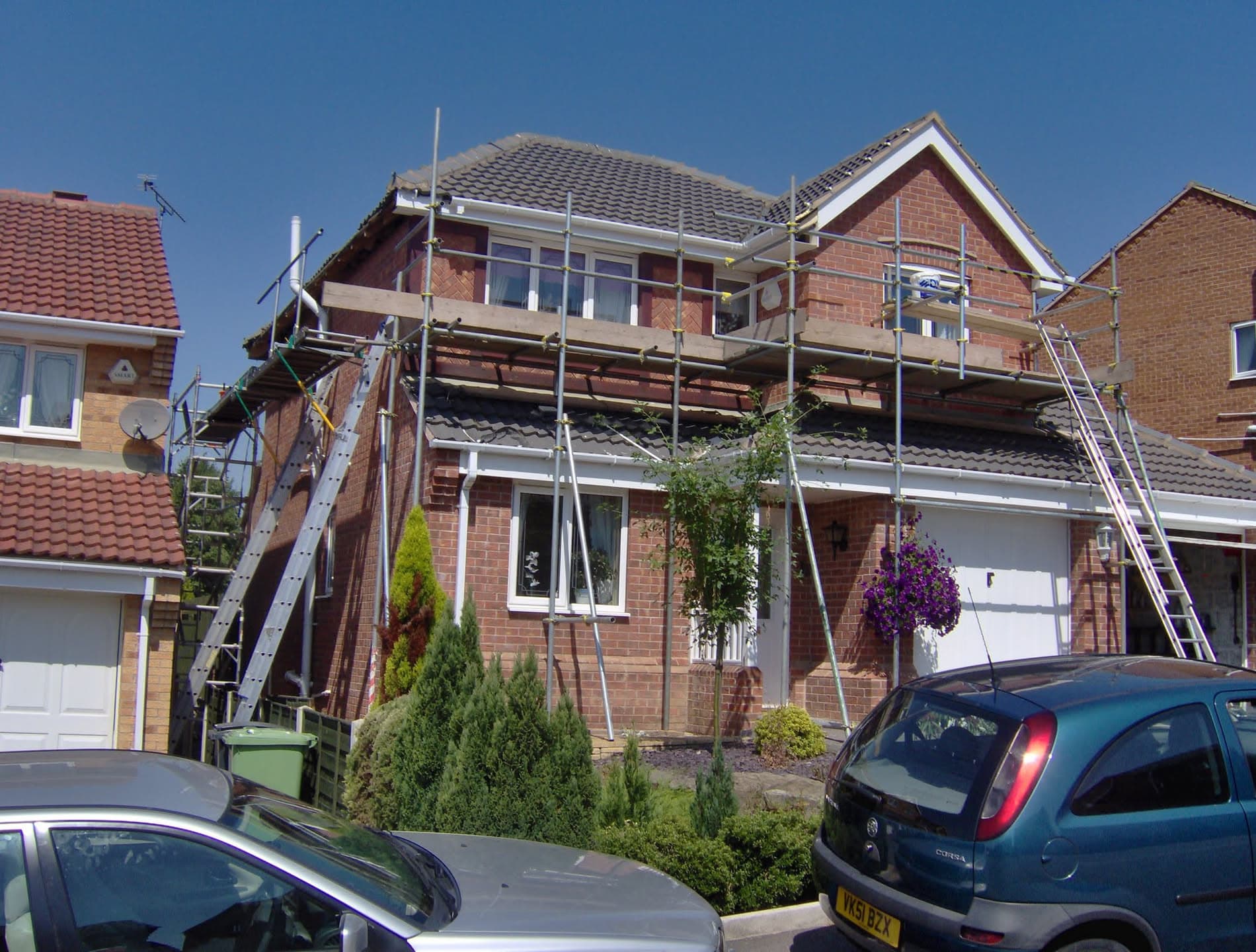 Pitched roof re-tiling work on red brick house with scaffolding erected around upper storey