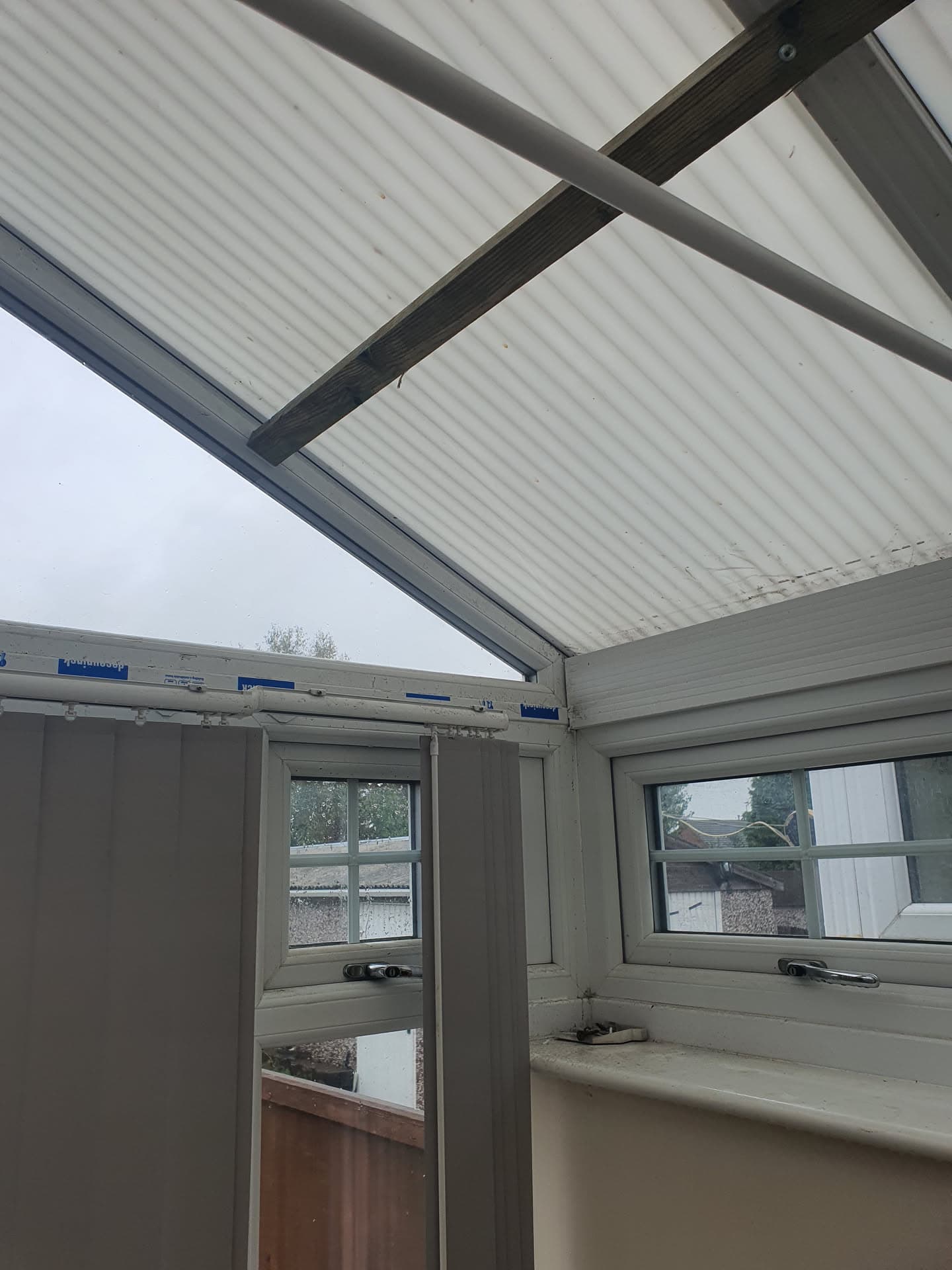 Interior view of conservatory with white corrugated polycarbonate roof panels and dark supporting beams