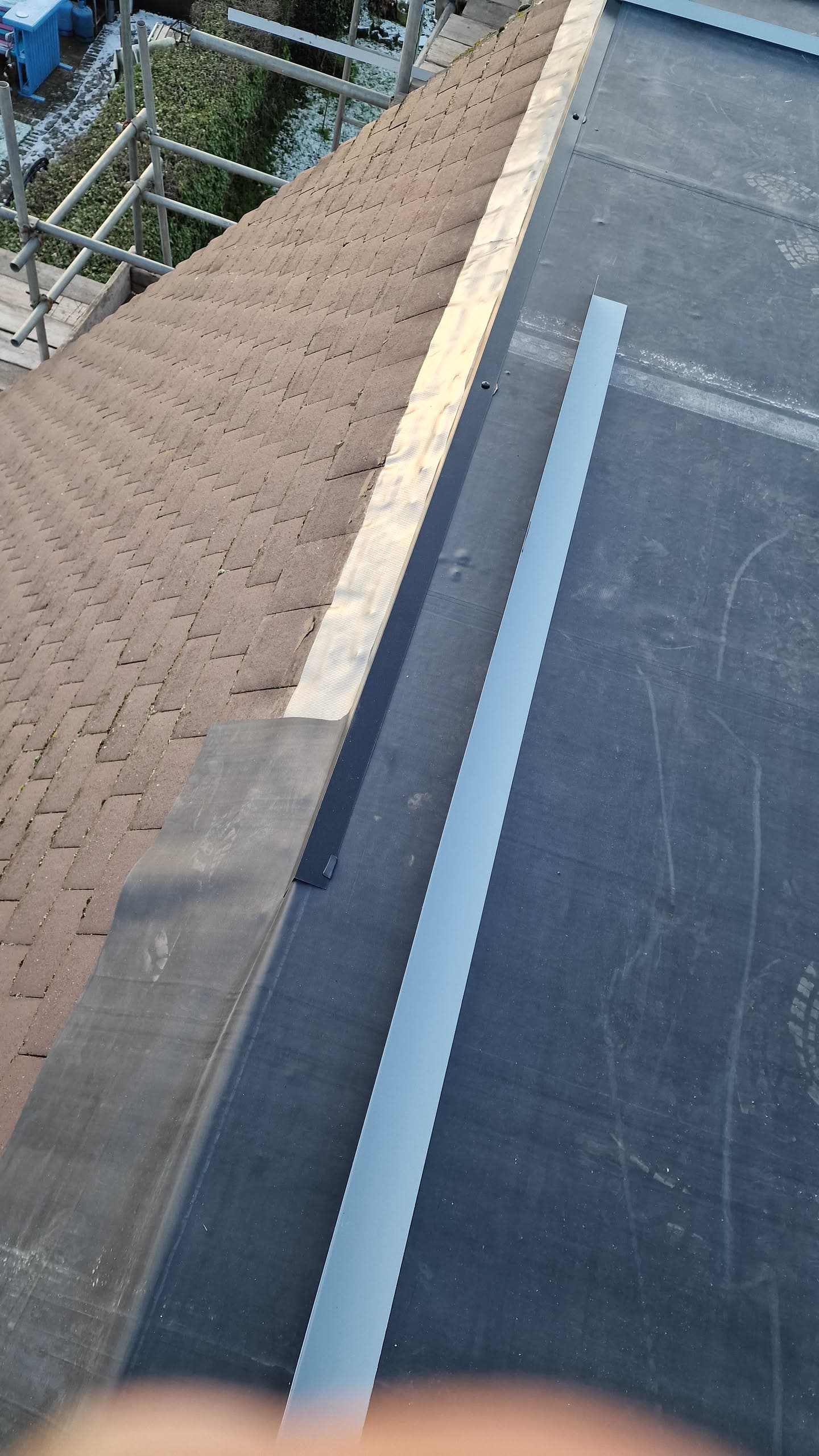 Pitched roof with brown concrete tiles meeting flat roof with grey felt and lead flashing, scaffolding visible