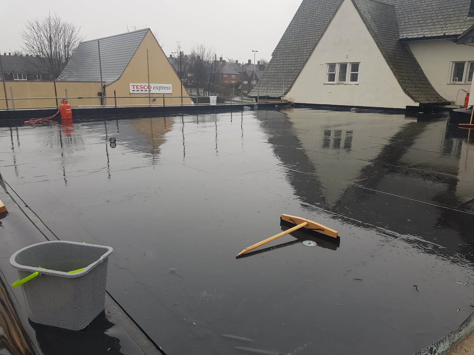 Large commercial flat roof with dark EPDM rubber membrane, wet from recent rain