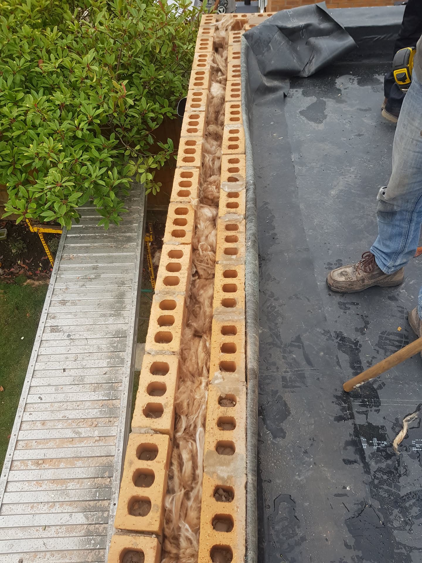 Flat roof installation with grey felt membrane and cavity wall insulation visible