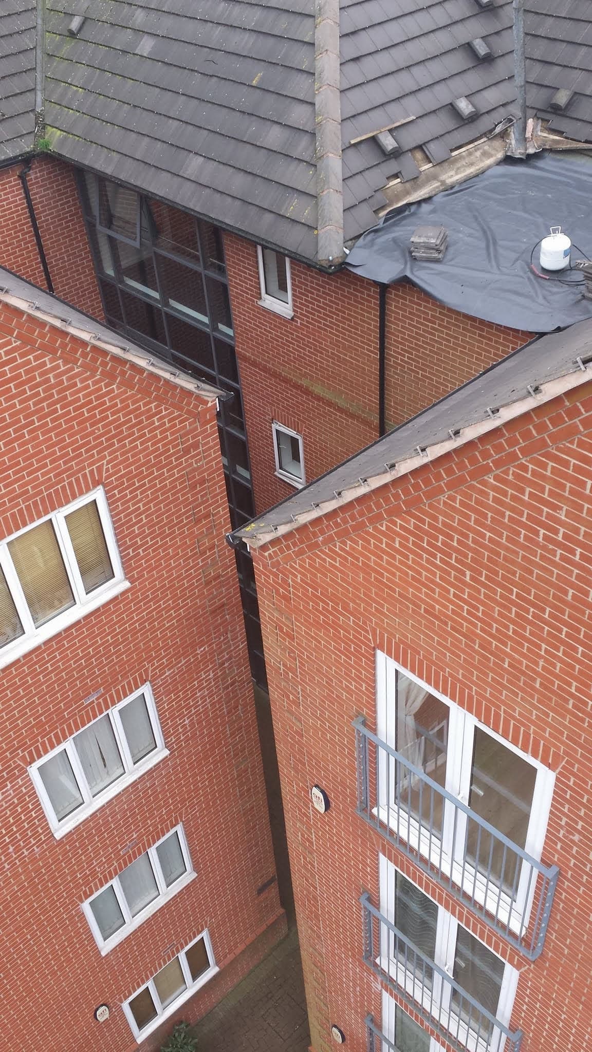 Grey tiled pitched roof and flat roof section on brick apartment building