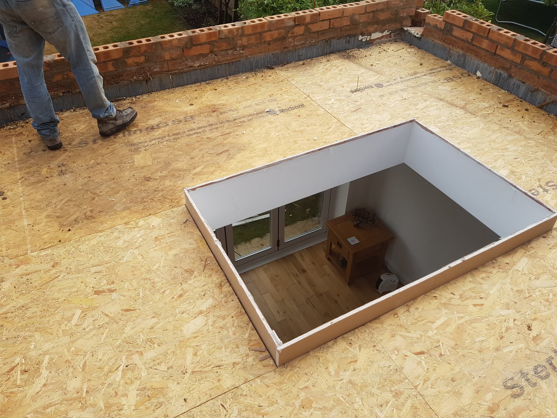 Flat roof installation in progress with timber-framed rooflight opening and OSB decking