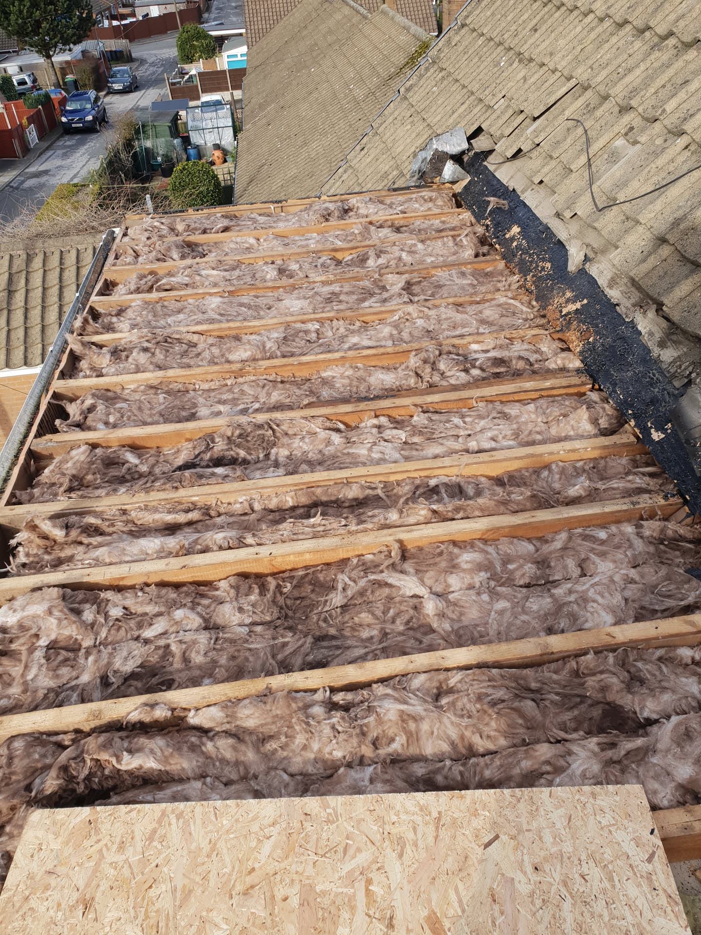 Pitched roof with exposed timber battens and insulation during re-roofing work, adjacent concrete tiled roof visible