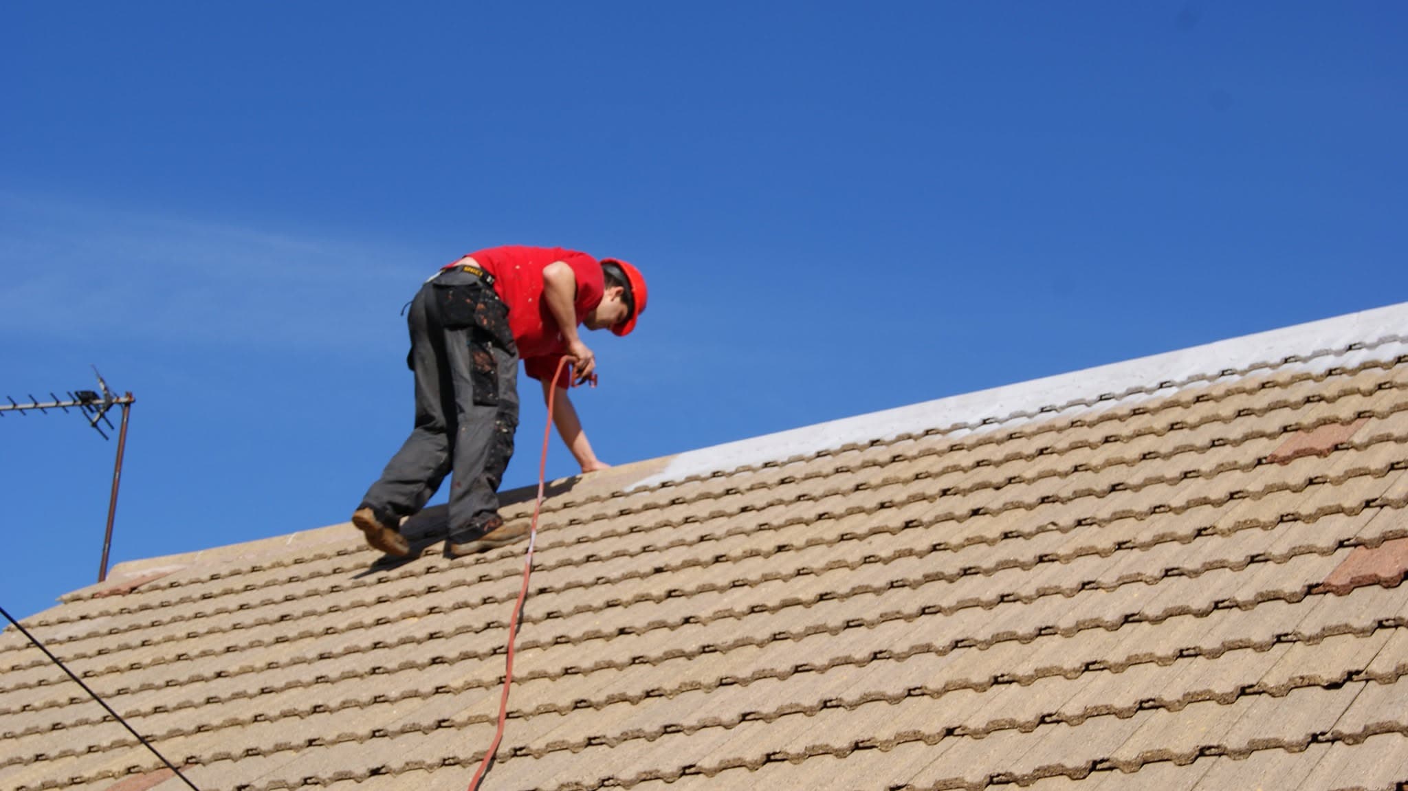 Roofer in red shirt working on pitched concrete tiled roof