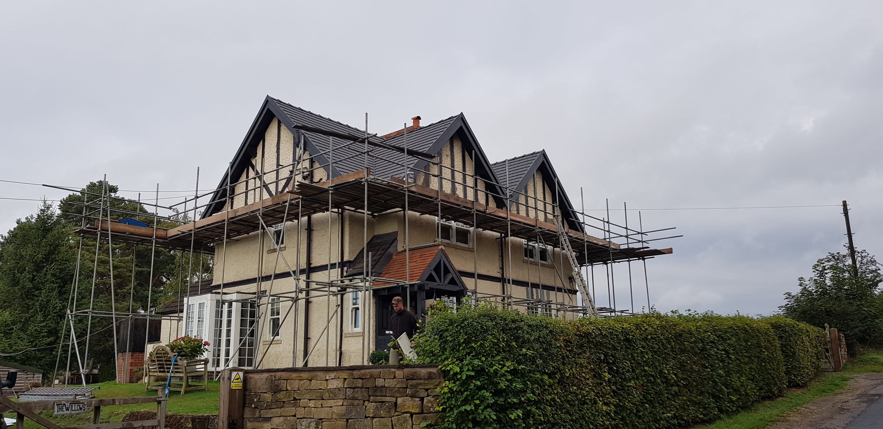 Pitched roof with dark grey tiles and chimney stack, scaffolding erected around property