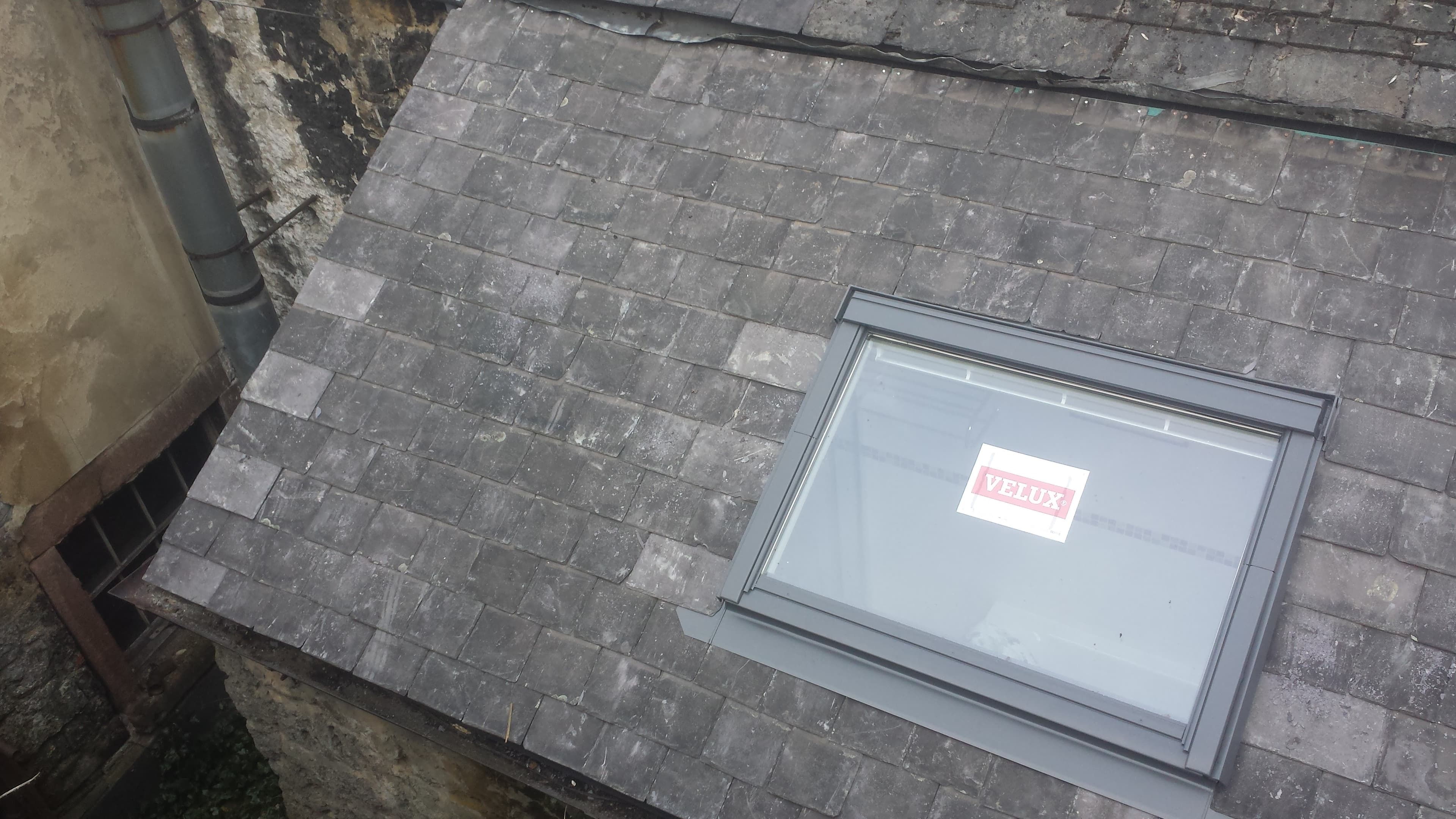 Grey slate pitched roof with Velux roof window and guttering