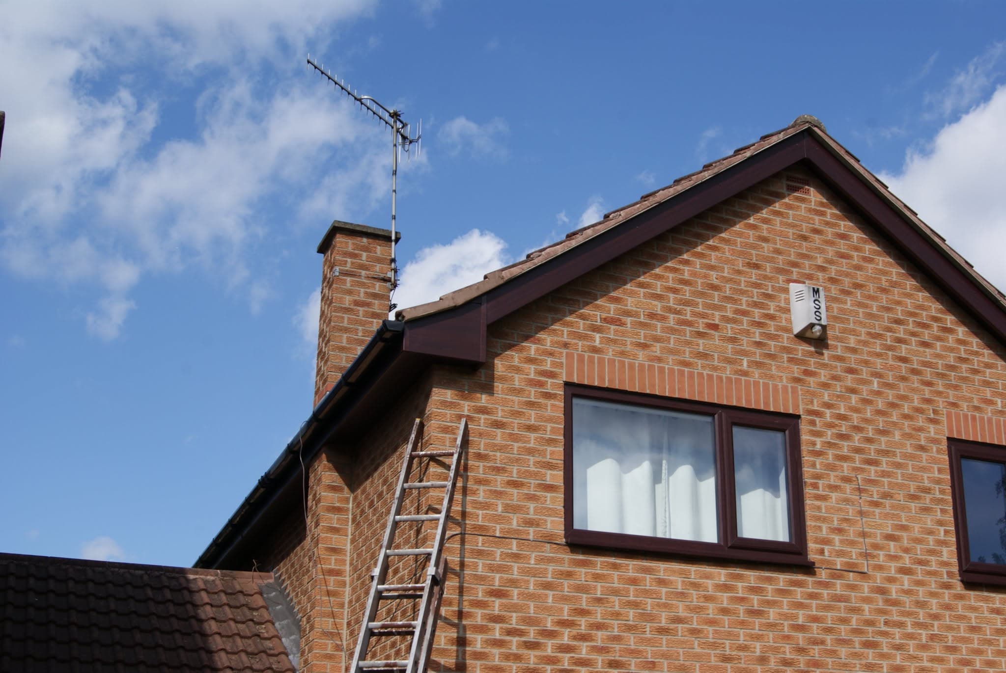 Pitched roof with brown concrete tiles, brown fascias and guttering on brick house with chimney