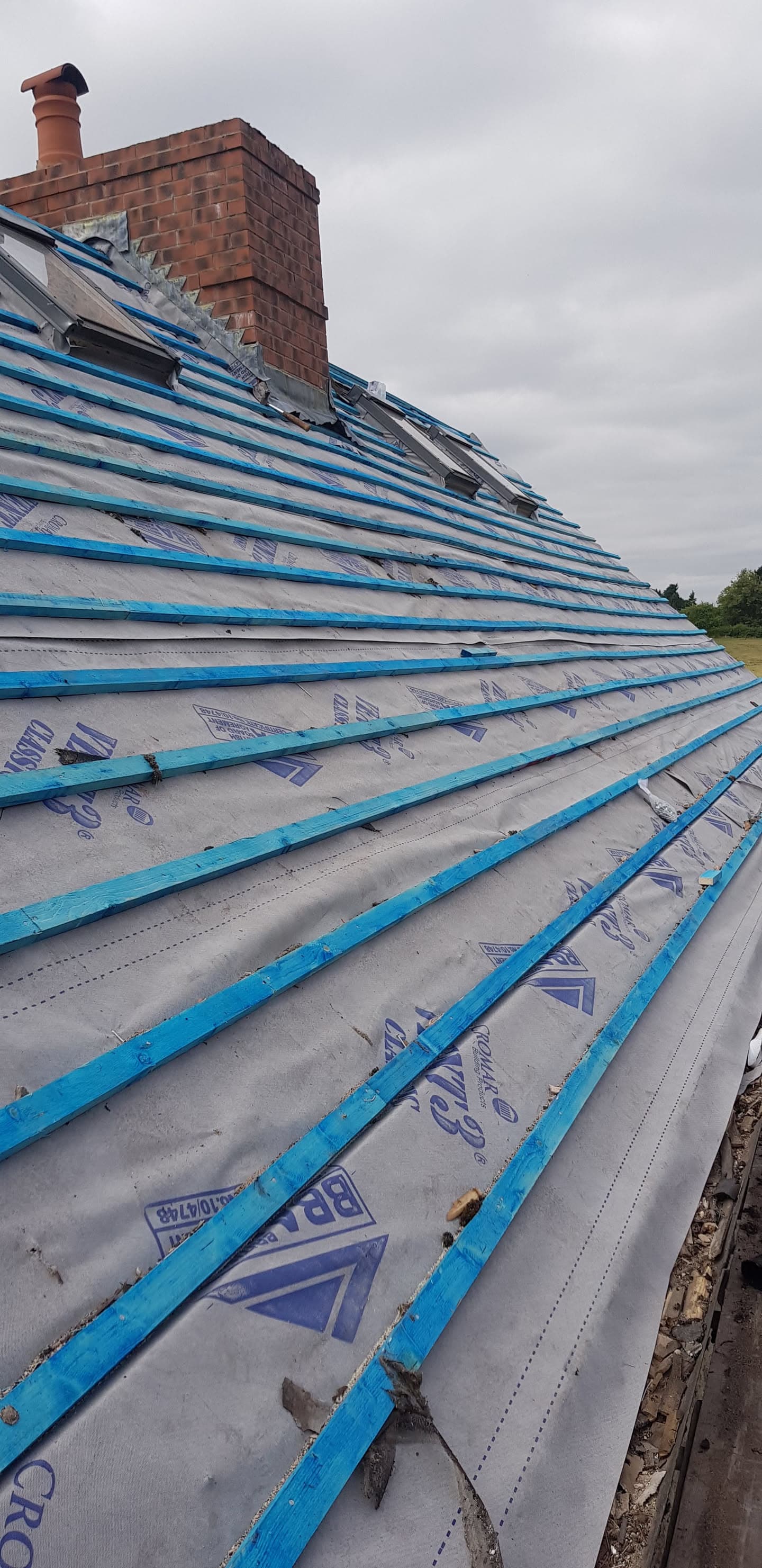 Pitched roof with blue battens and roofing membrane installed, brick chimney stack visible