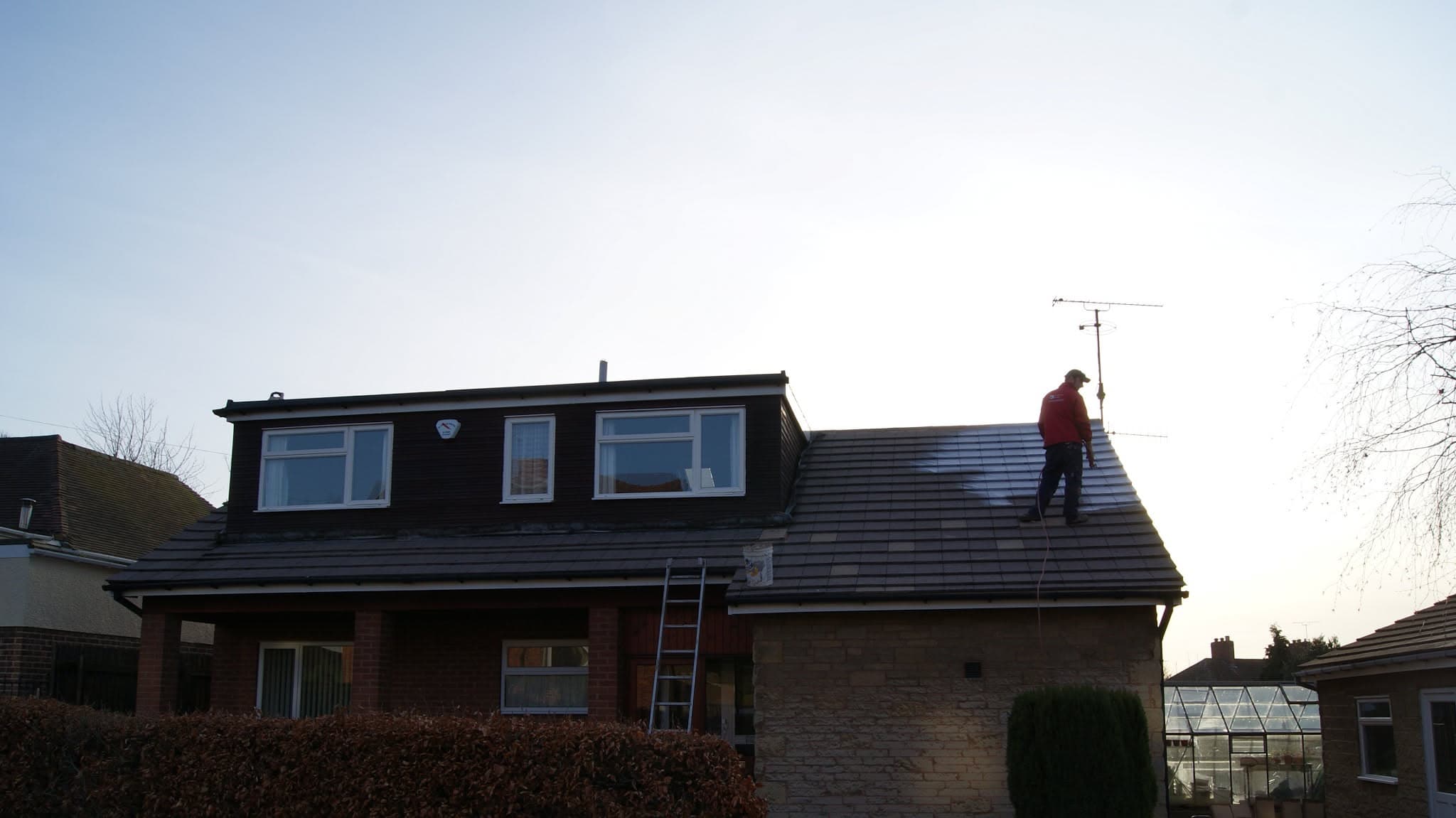 Fitter working on pitched tiled roof with ladder against property