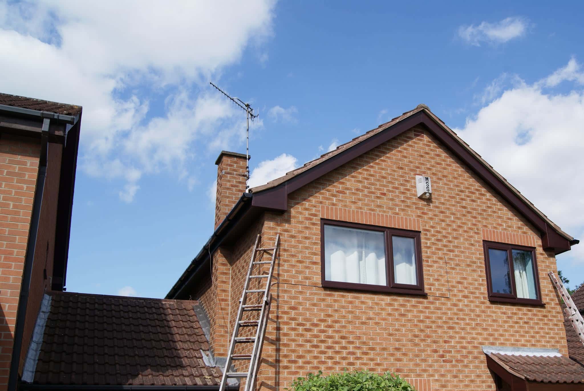 Pitched roof with brown concrete tiles, dark fascias and chimney stack with aerial
