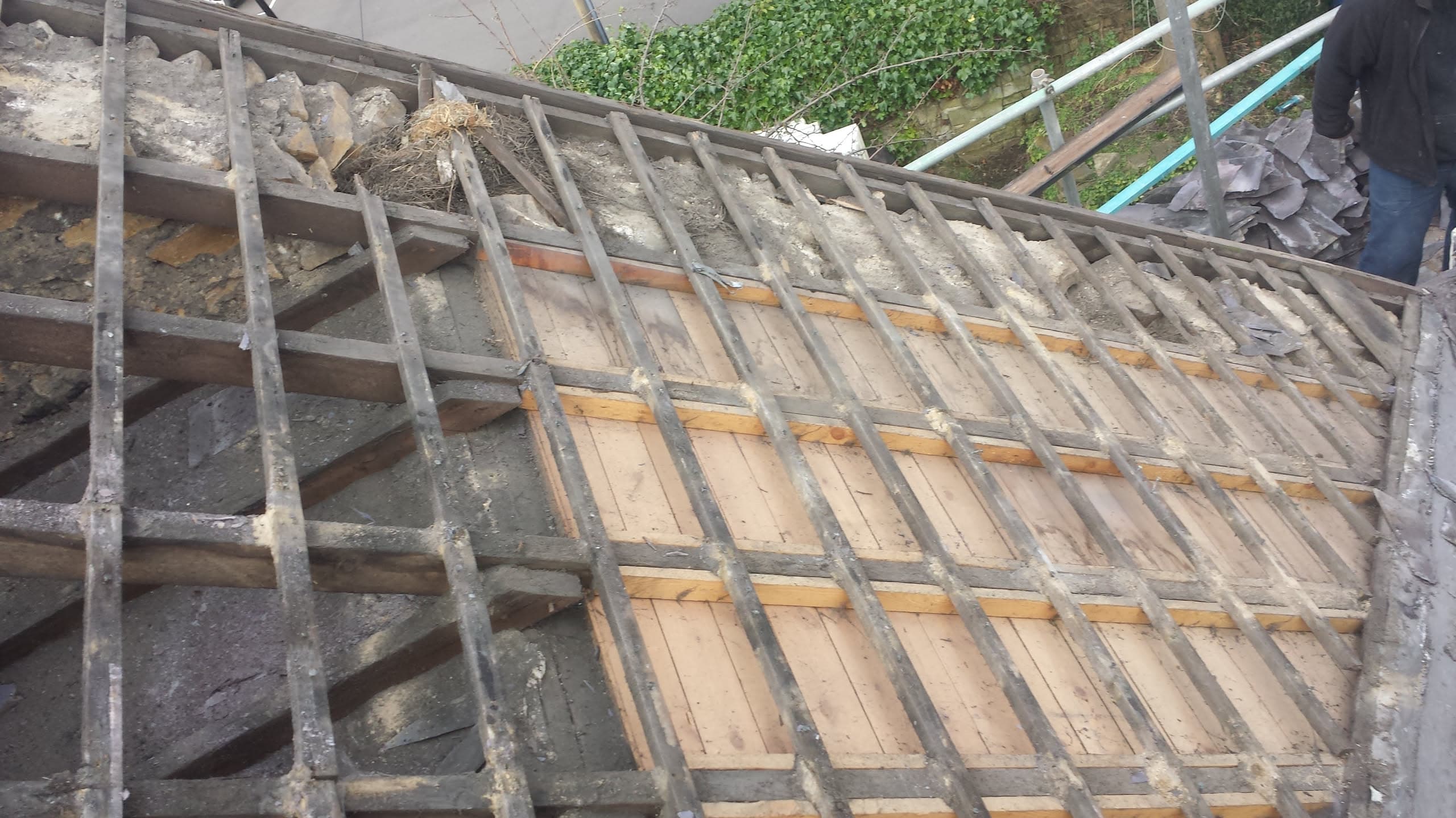 Pitched roof stripped to timber battens during re-roofing work with fitter visible
