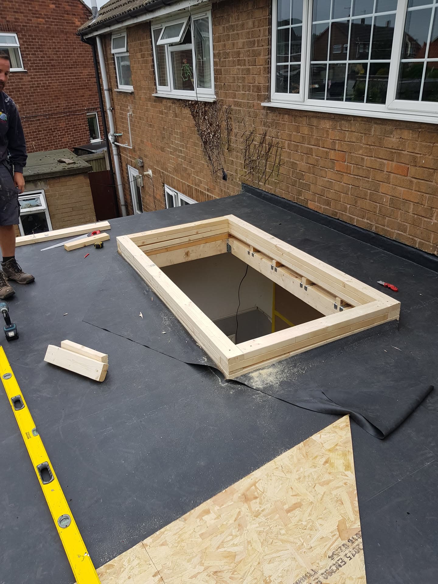 Flat roof with felt covering and timber skylight frame being installed by fitter