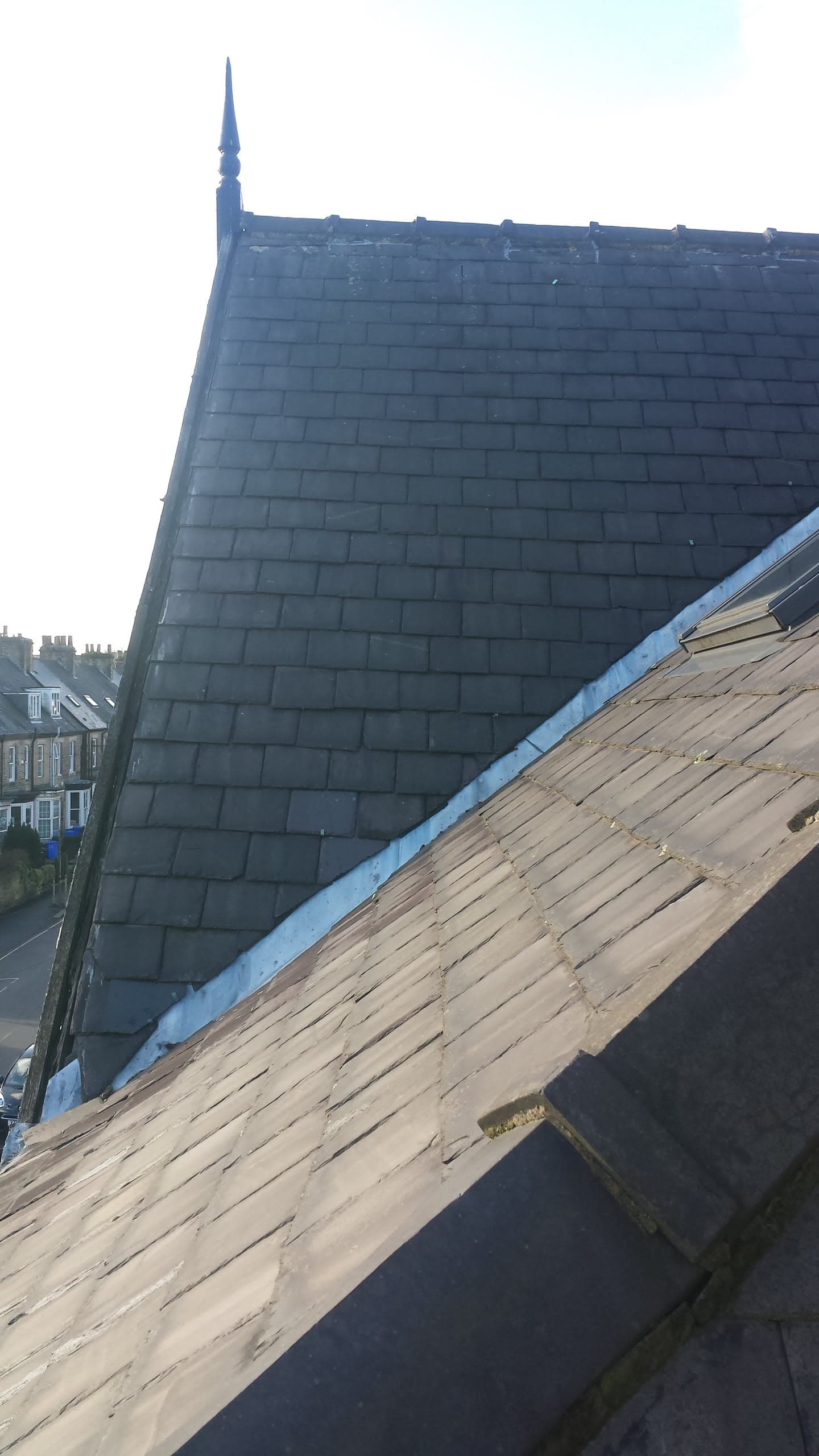 Pitched slate roof with decorative finial and exposed timber decking on adjacent roof section