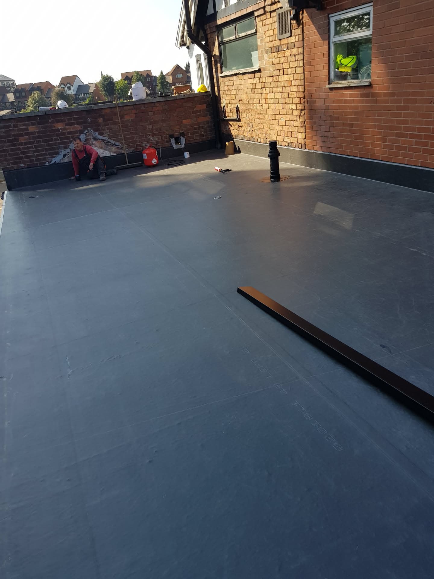 Newly installed grey EPDM rubber flat roof with fitter working in background