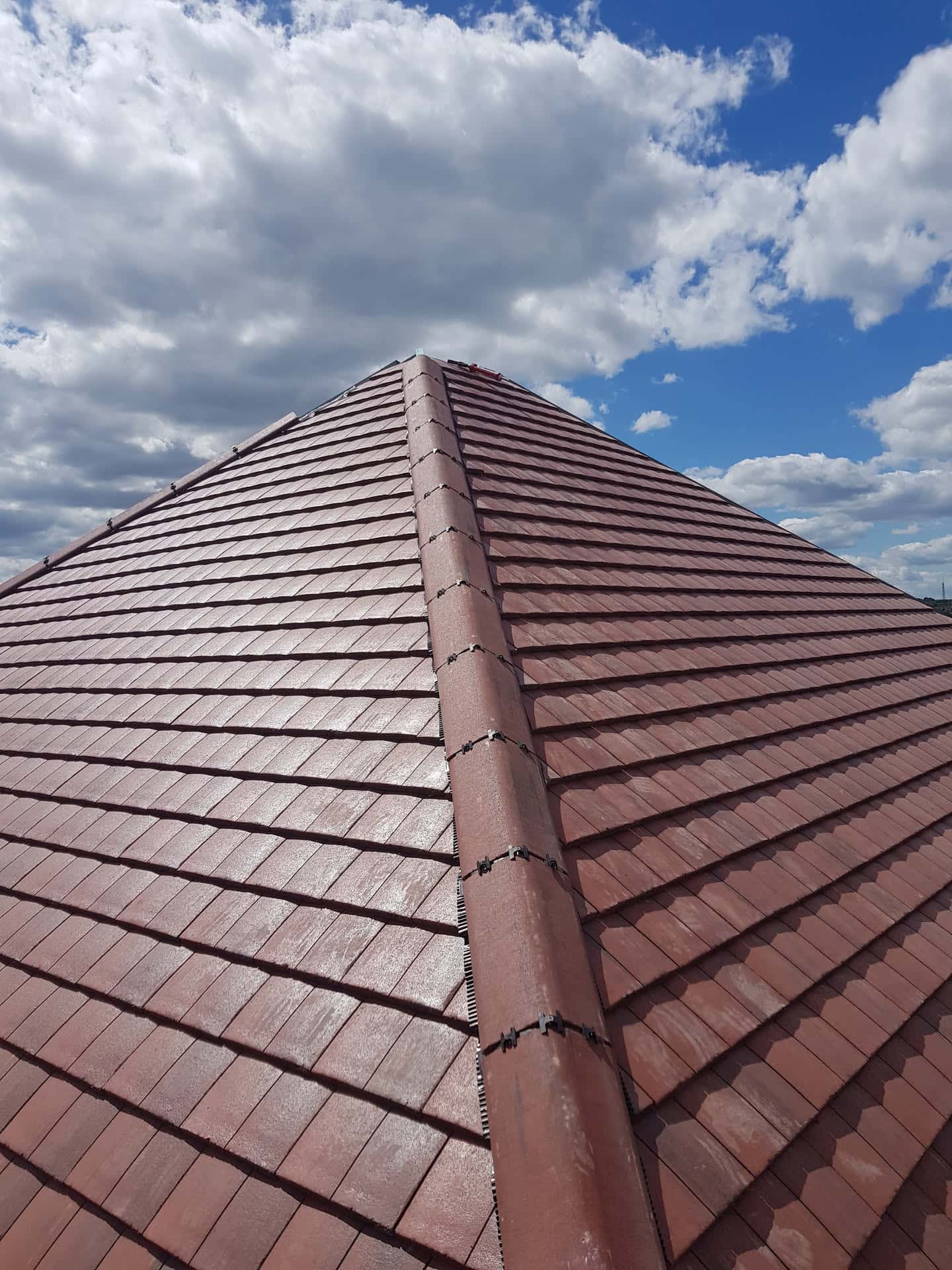 Newly completed pitched roof with brown concrete tiles and ridge capping