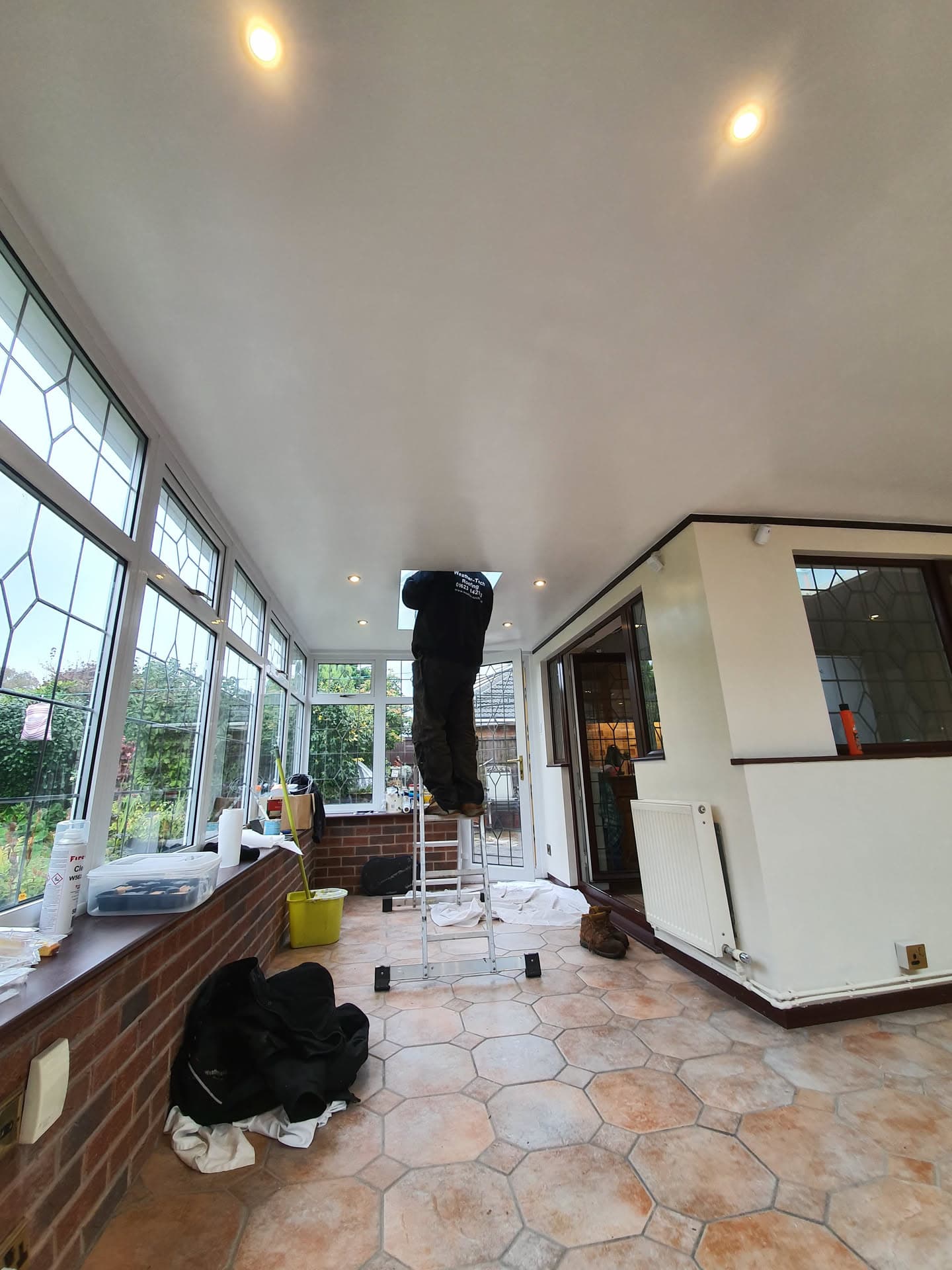 Fitter installing white ceiling panels inside conservatory with glazed roof and walls