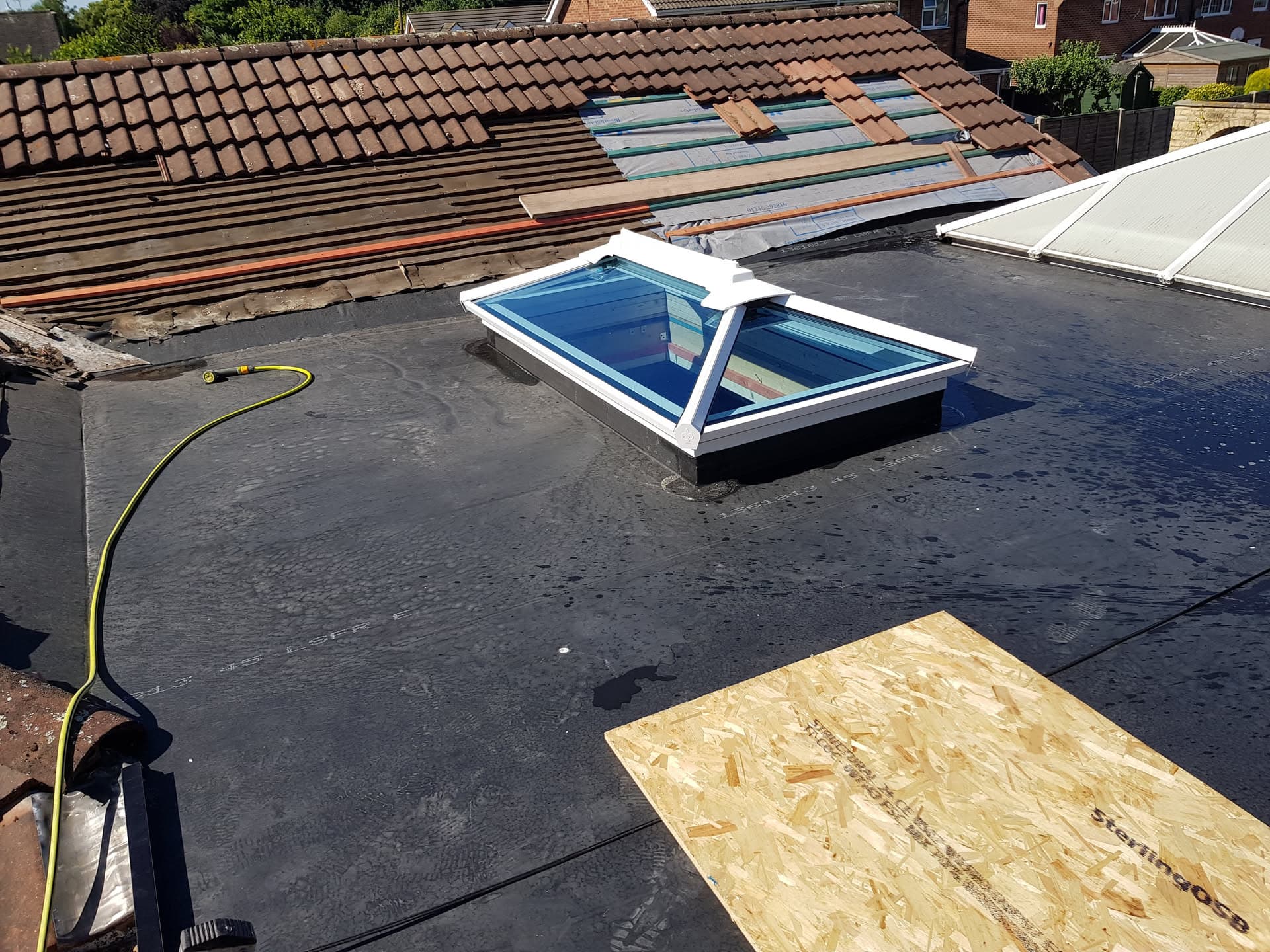 Flat roof with GRP fibreglass surface and white-framed roof lantern, adjacent to brown tiled pitched roof