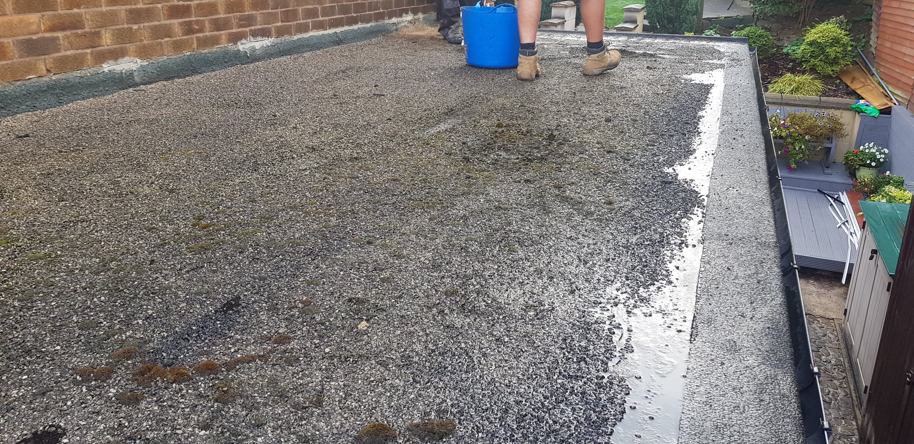 Flat roof with grey felt surface being installed, fitter visible working on roof
