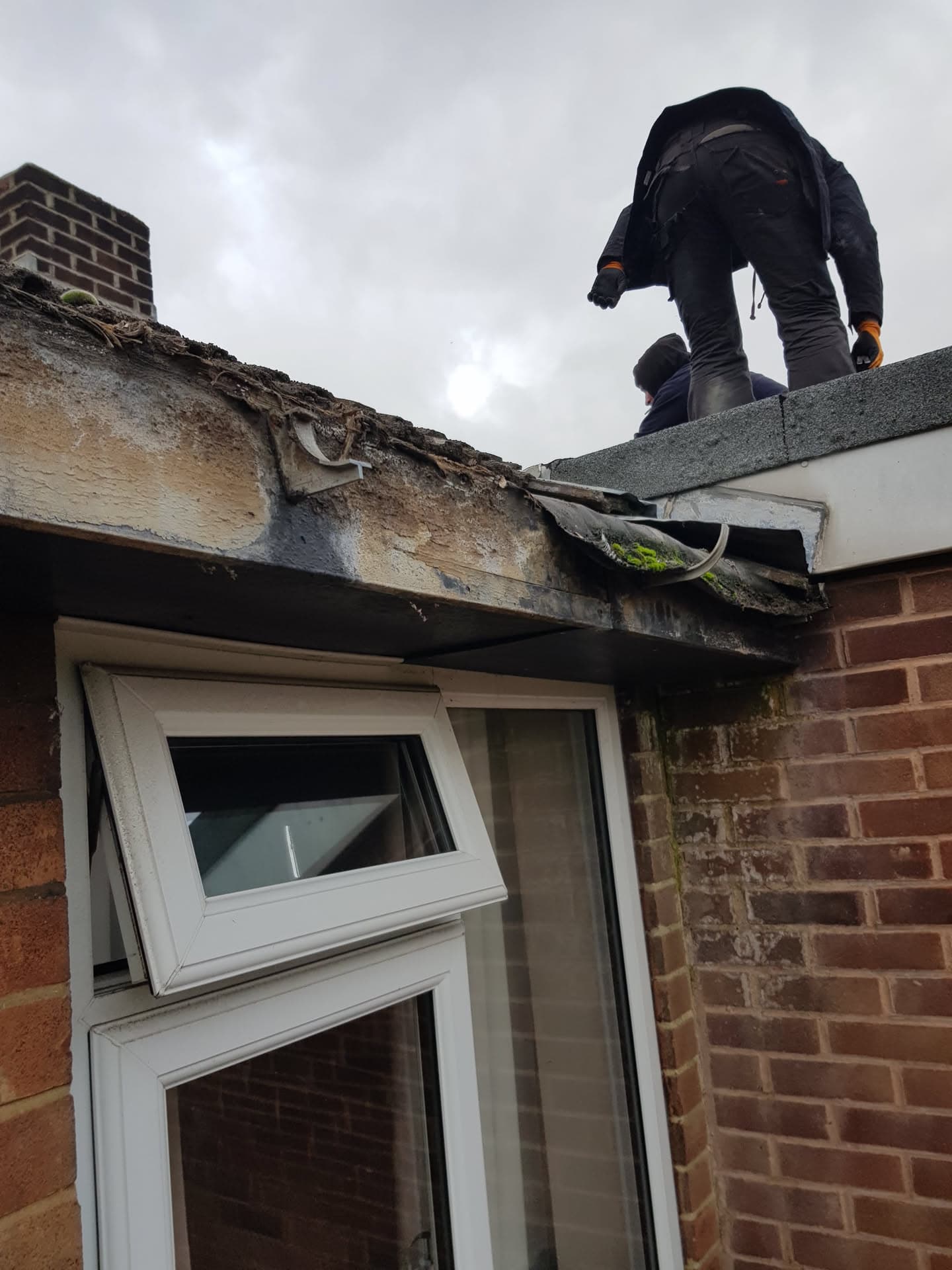 Roofer working on damaged flat roof with deteriorated fascia and guttering