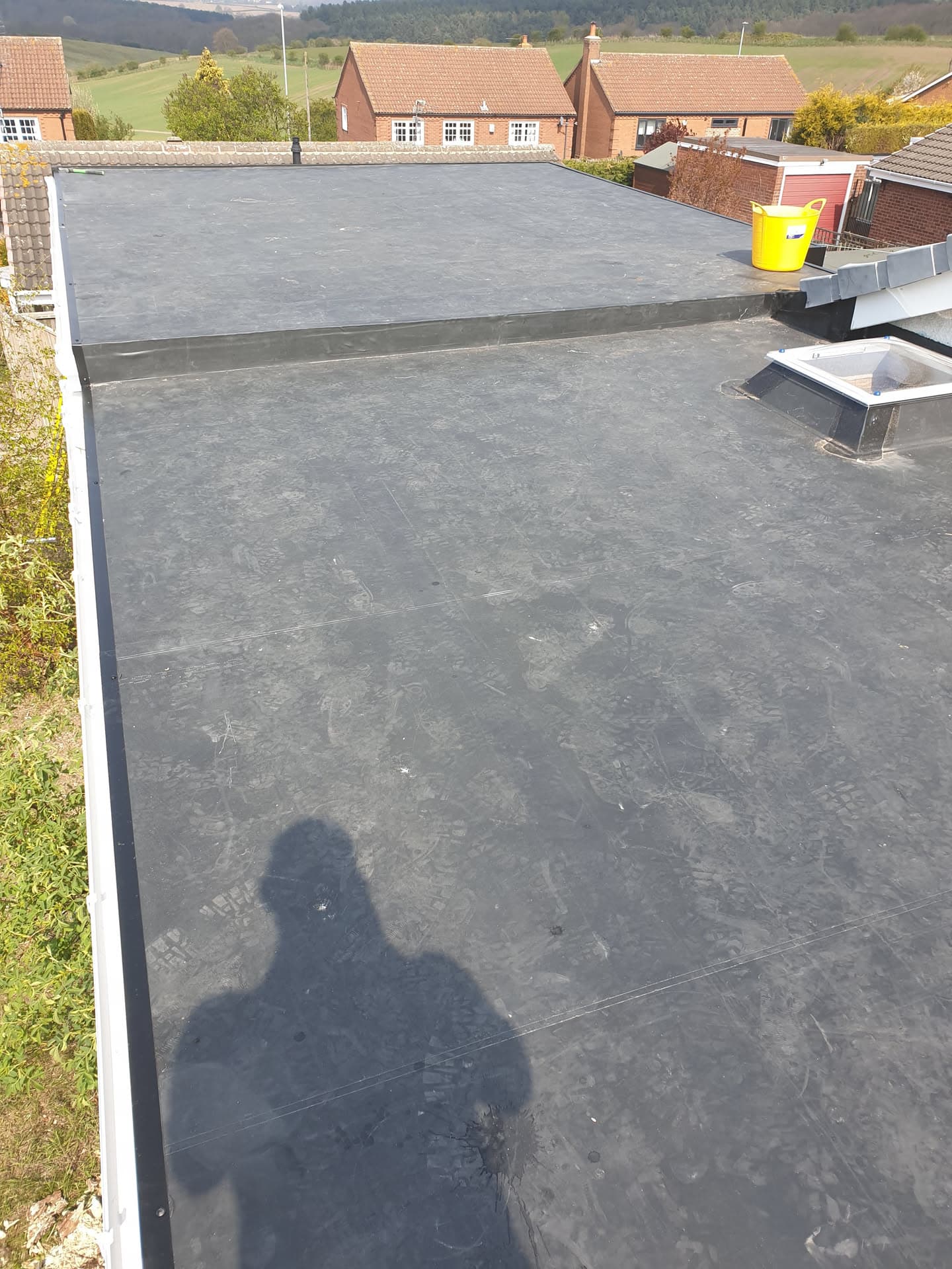 Completed flat roof installation with dark grey felt membrane and skylight