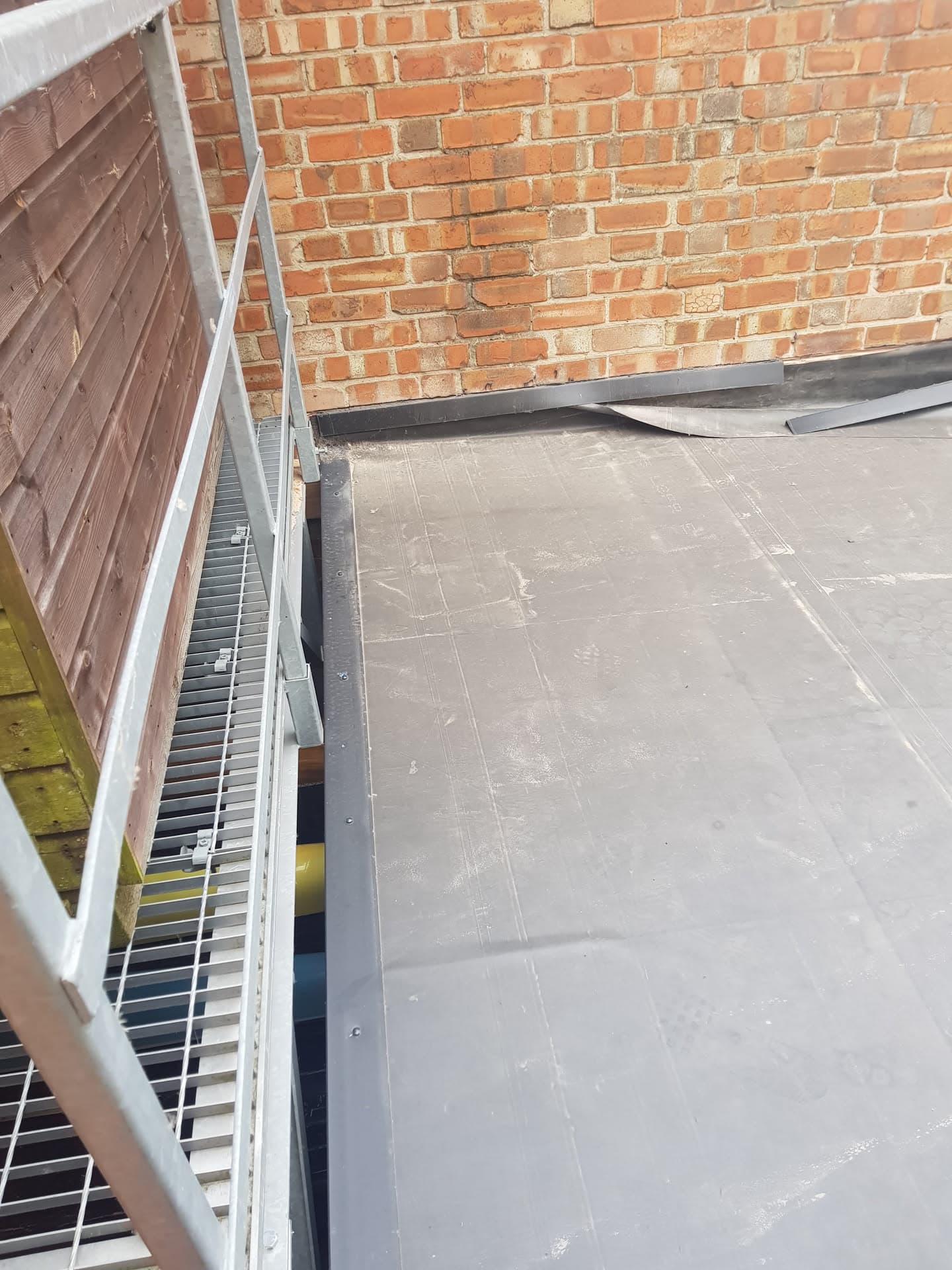 Flat roof with grey felt covering and lead flashing against brick wall