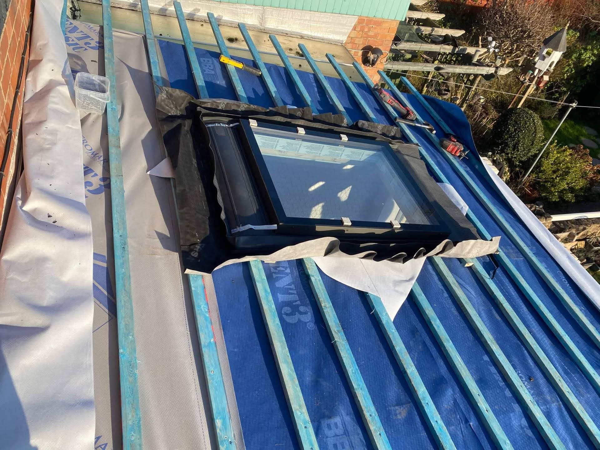 Blue corrugated metal roof installation in progress with Velux roof window being fitted