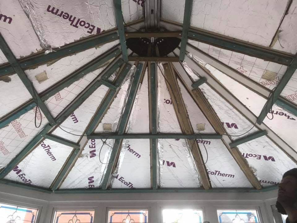 Interior view of conservatory roof structure with green framework and insulation panels during installation