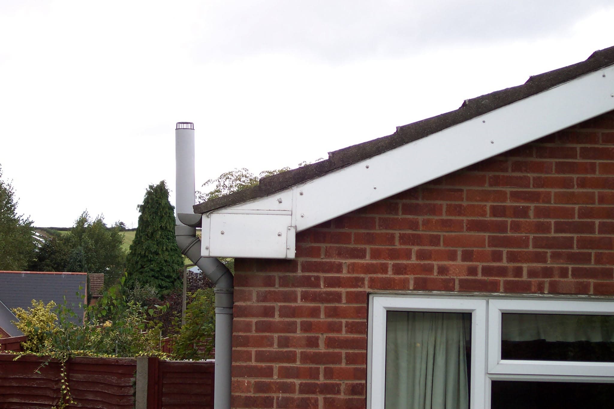 Pitched roof with dark concrete tiles, white fascia board and grey downpipe