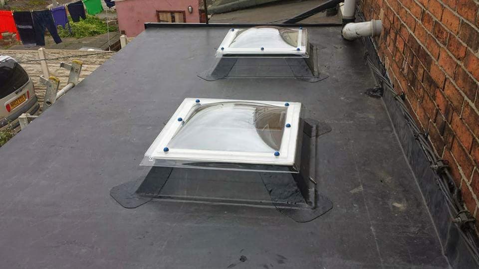 Flat roof with two white-framed roof lanterns installed on grey felt covering