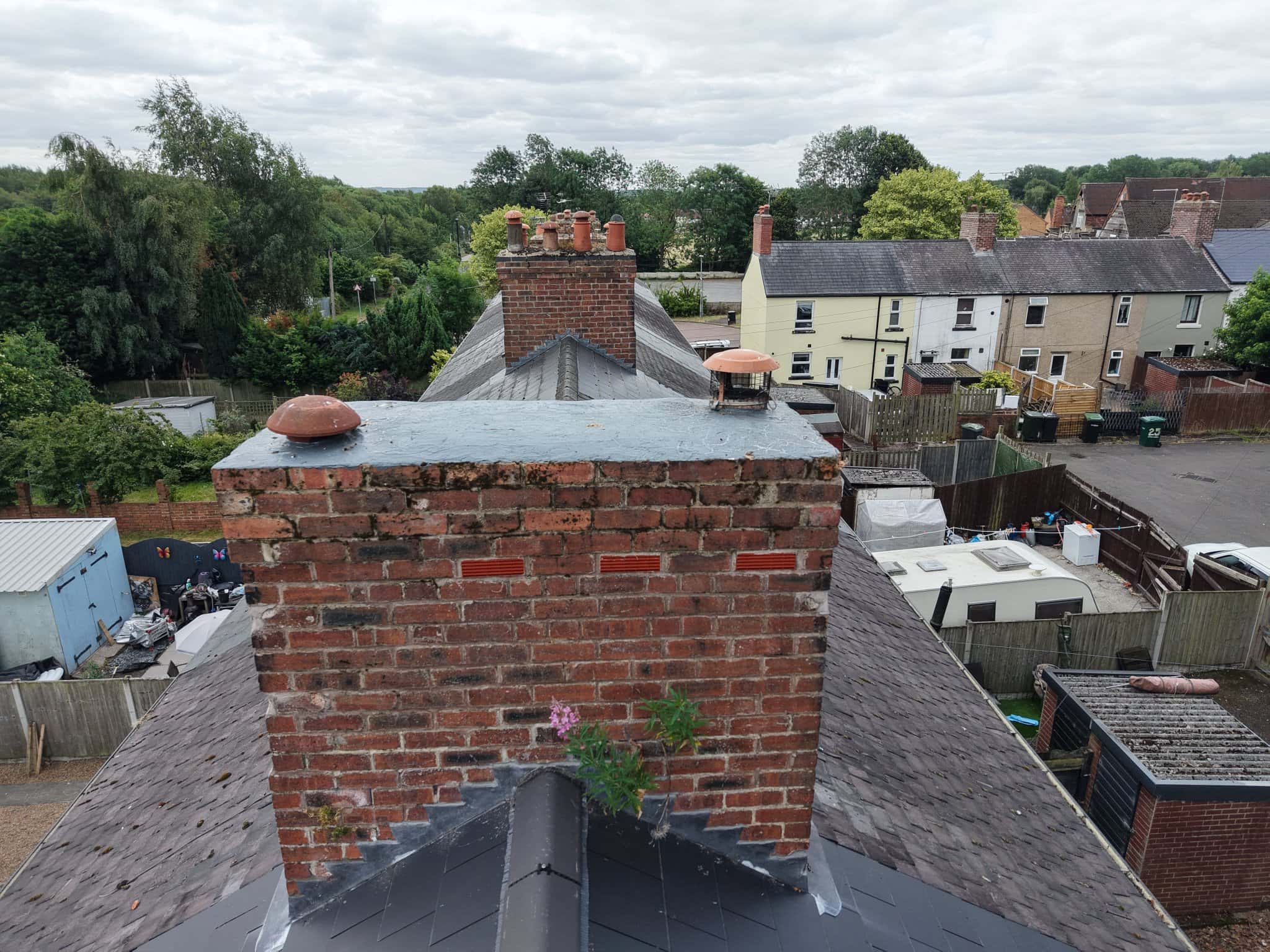 Drone survey photo of a weathered brick chimney stack with eroded mortar joints and a weed growing from the brickwork at ridge height